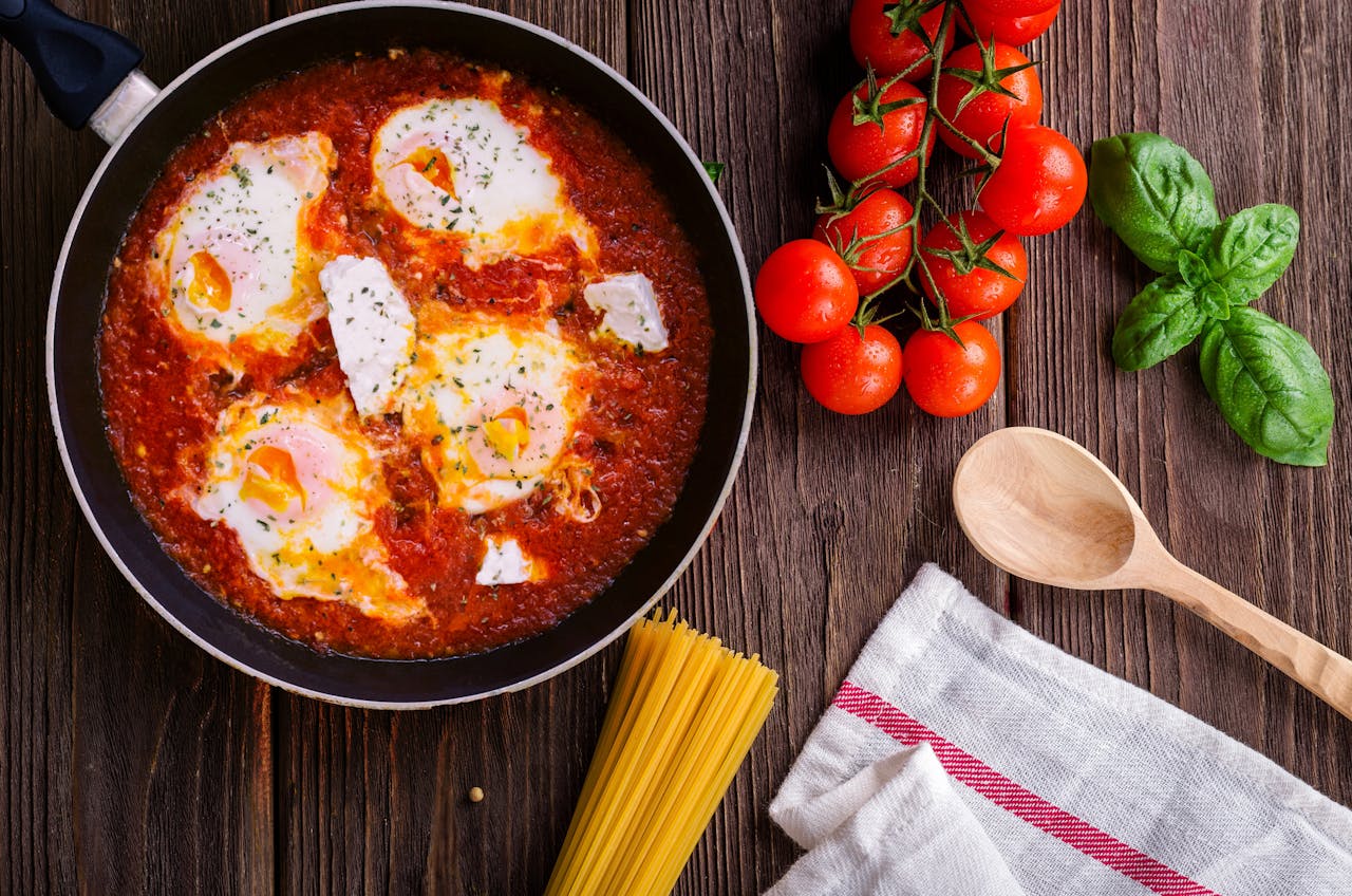 Home Delicious eggs in tomato sauce with basil, spaghetti, and fresh tomatoes on a wooden table.