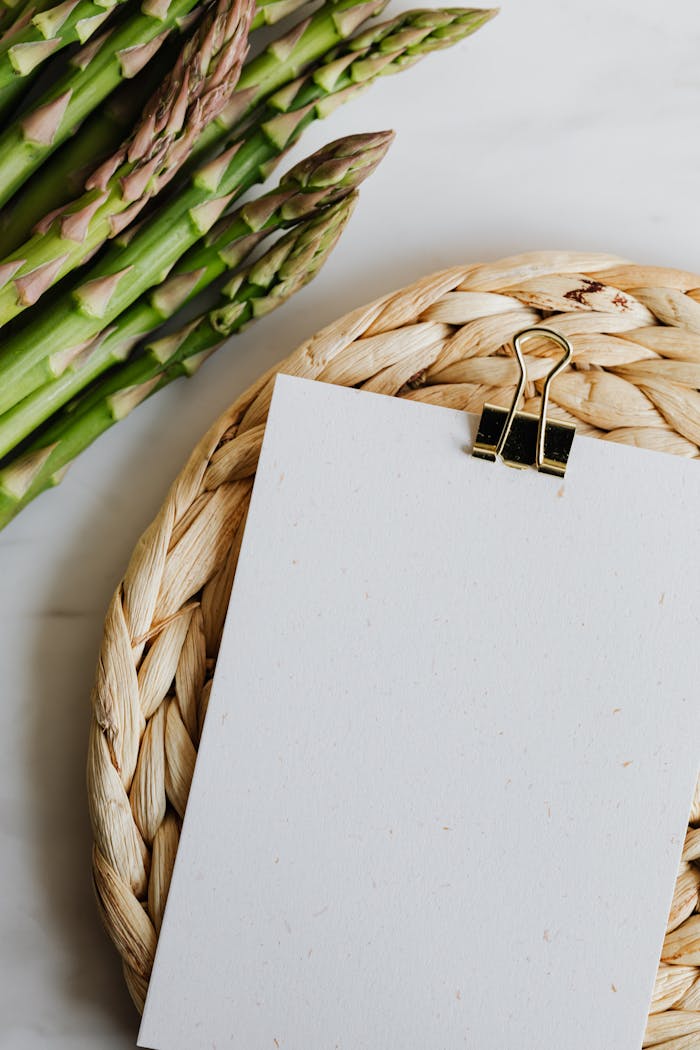 Services Fresh asparagus stalks next to blank paper on a wicker mat, perfect for culinary content.